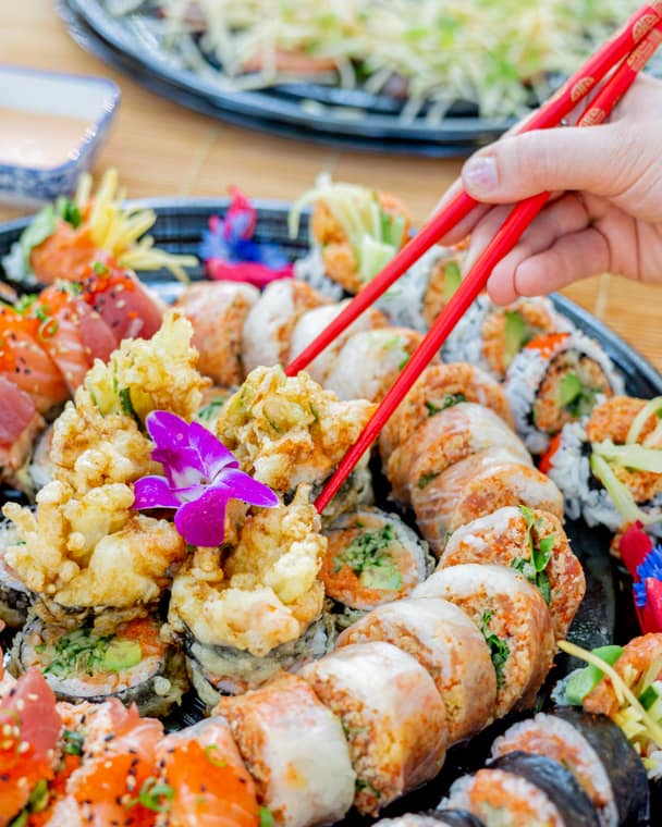 Sushi platter with tempura rolls and orchids, served with red chopsticks