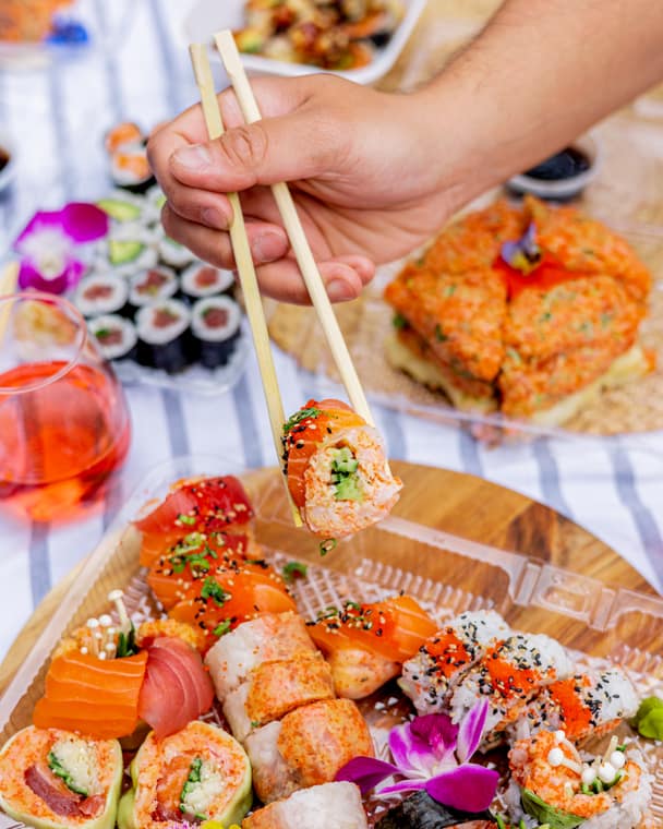 Chopsticks lifting a roll from a colourful sushi spread